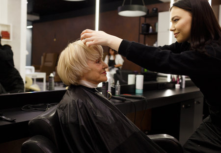 Portrait of an elderly woman visiting a professional hairdresser. An experienced hairdresser does hair styling for a clientの写真素材