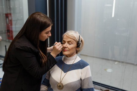 An elderly woman visiting a professional makeup artist. An makeup experienced artist does makeup for a client.の写真素材
