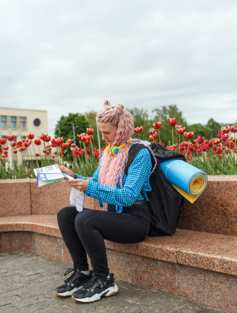 An attractive young tourist in a blue shirt is exploring a new city. A girl with long pink hair holds a paper map of the city scheme in her hands. Travel around Europeの写真素材