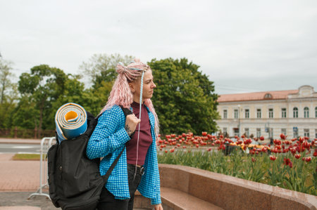 a girl with headphones and pink hair is traveling around the city with a backpack on her shoulders. Talking on the phone.の写真素材