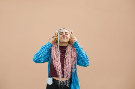 Portrait of a young woman with pink long hair and a blue shirt. A girl with headphones on a bright...