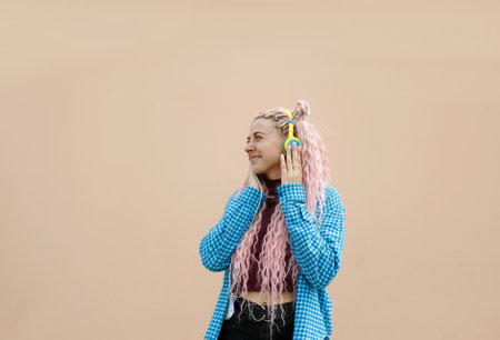 A happy young woman with pink long hair and a blue shirt. A girl with headphones on a bright background. Empty space for advertising text.の写真素材
