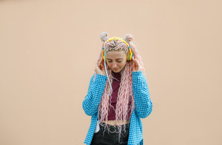 A happy young woman with pink long hair and a blue shirt. A girl with headphones on a bright background. Empty space for advertising text.の写真素材