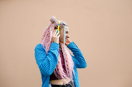A happy young woman with pink long hair and a blue shirt. A girl with headphones on a bright...