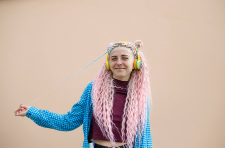 A happy young woman with pink long dreadlocked hair and a blue shirt. A girl in yellow headphones on a bright background. Empty space for advertising text.の写真素材