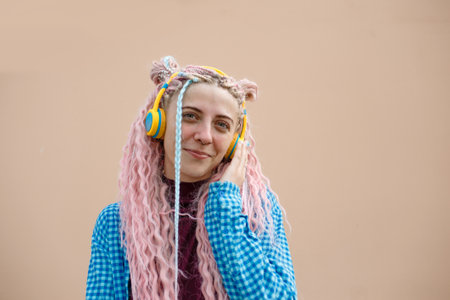 A happy young woman with pink long hair and a blue shirt. A girl with headphones on a bright background. Empty space for advertising text.の写真素材