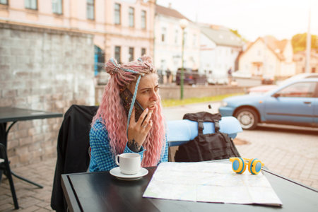 An attractive young tourist in a blue shirt is exploring a new city. A girl with long pink hair is having lunch in a cafe. Travel around Europeの写真素材