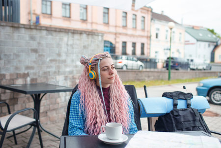 An attractive young tourist in a blue shirt drinks coffee and listens to music with headphones. A girl with long pink hair is having lunch in a cafe. Travel around Europeの写真素材