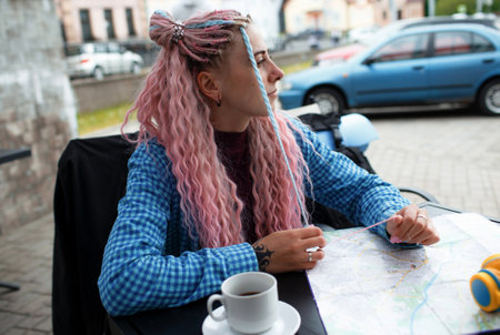 An attractive young tourist in a blue shirt drinks coffee and listens to music with headphones. A girl with long pink hair is having lunch in a cafe. Travel around Europeの写真素材