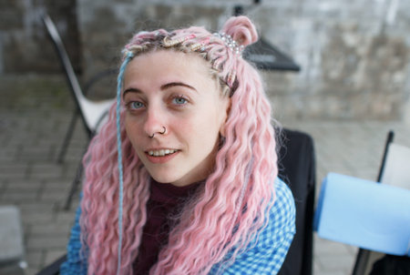 An attractive girl with pink hair and a blue shirt drinks coffee and listens to music sitting at a...