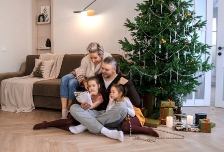 Portrait of a friendly family reading a book sitting on the floor near the Christmas treeの写真素材