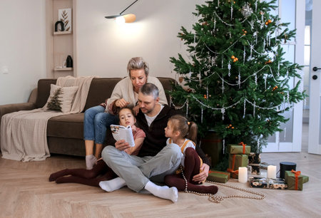 Portrait of a friendly family reading a book sitting on the floor near the Christmas treeの写真素材