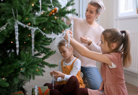 Mom and daughters decorate a Christmas tree sitting on the floor in the living roomの写真素材