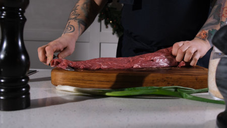 The cook cuts beef meat with a knife on a cutting board. The chef separates the entrecote from a piece of fresh meatの写真素材