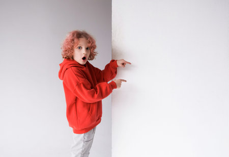 A red-haired boy in a red sweater points his finger at an empty white board, a place for...