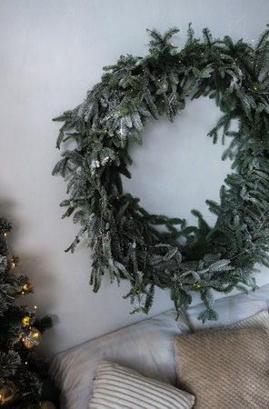 A large, frosted Christmas wreath with warm fairy lights hangs on a wall above a bed with cozy pillows. The wreath s lush greenery and soft glow create a festive and inviting atmosphere, perfect for the holiday season.の写真素材
