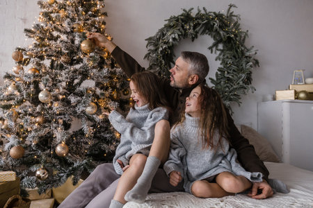 A father and his two daughters create lasting holiday memories while decorating a stunning Christmas tree. Their joy is infectiousの写真素材
