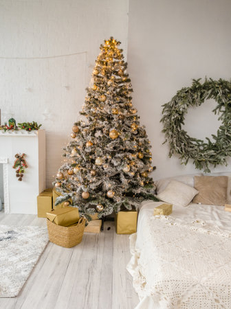A snow-dusted Christmas tree decorated with gold ornaments stands in a cozy room. Gifts are piled beneath. A neutral color scheme creates a calm and festive atmosphere.の写真素材