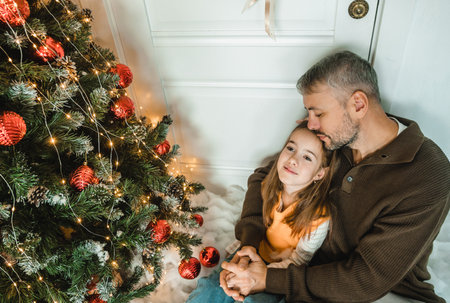 Father and daughter enjoying Christmas together. Gentle moment of affection near a decorated Christmas tree.の写真素材