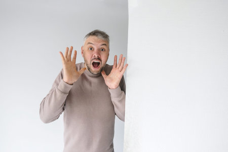 A surprised man with his mouth open and hands raised in shock. He s standing next to a blank white...