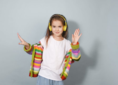 A cheerful girl wearing colorful striped cardigan and yellow headphones waves hello. She s...