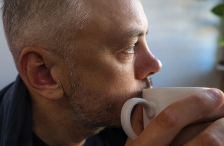 Close-up profile of a man enjoying a warm drink. His contemplative expression and the soft light create a mood of peaceful relaxationの写真素材