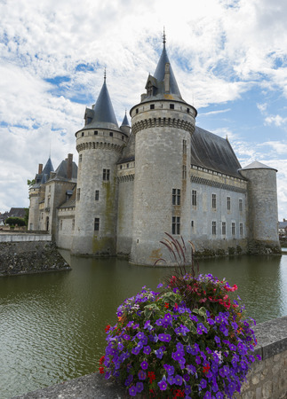Castle in Sully sur Loire in France with purple flowers and a canal.のeditorial素材