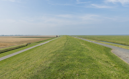 Grass dike in Groningen with wide landscap and blue sky.の写真素材