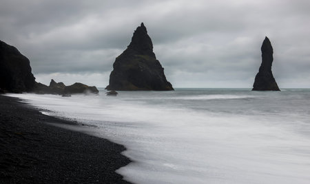 Reynishverfisvegur, Reynisfjara black sand beach with rocks,  ocean and dark rain and storm clouds...