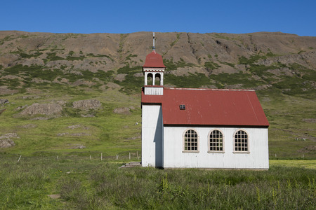 White church with red roof with mountains in the background at Gufudalur-Nedri on Iceland.の写真素材