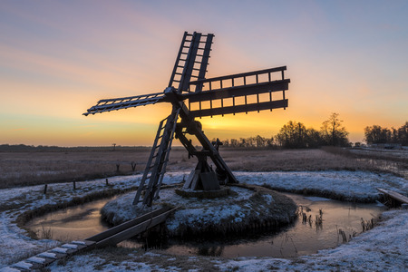 Tsjaker near Kalenberg during sunrise in wintertime with snow, trees and ditch in National Park De Weerribben-Wieden in The Netherlands.の写真素材
