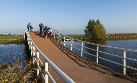 Groot-Ammers, The Netherlands - November 11, 2016: Modern architecture of a cycling bridge over a small canal with three cyclists at Groot-Ammers in the Netherlands.のeditorial素材