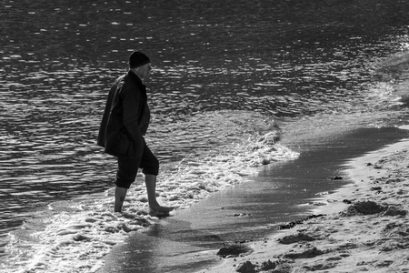 Saint Ives, England - April 27, 2017: Man with jacket walking on the beach in Saint Ives on his bare feet, Cornwall, England.のeditorial素材