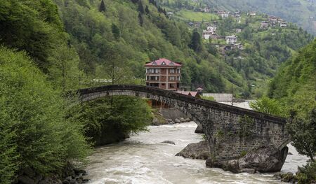 Muratkoy, Turkey - May 8, 2019: Old Ottoman arch bridge over the Firtina river with houses in the valley.のeditorial素材