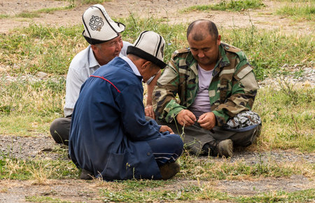 Osh, Kyrgyzstan - June 30, 2019: Three men sitting on the ground with ak-kalpak hat on the livestock...