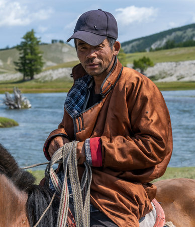 Khatgal, Mongolia - August 14, 2019: Mongolian shepherd on horseback with hat and on the steppe of...