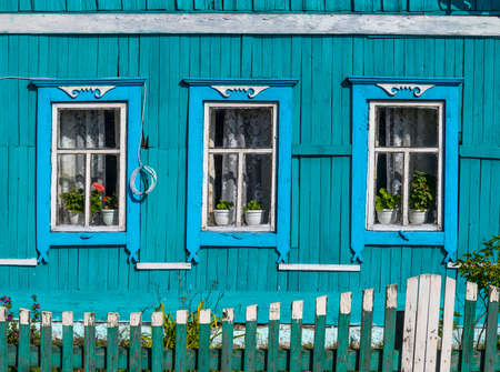 Russian old blue log cabin with green fence and some flowers in Tinskoy, Siberia, Russia.の写真素材