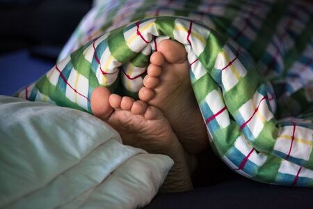 Small woman's feet under a blanket with colored patternの写真素材