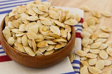 Toasted pumpkin seeds scattered against a table and striped towel with shallow depth of fieldの写真素材