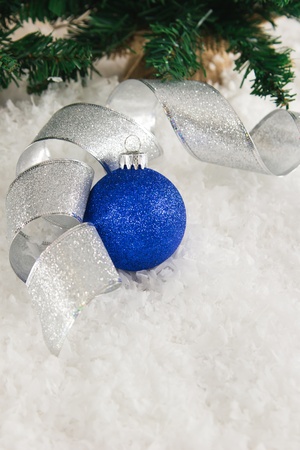 Sparkly silver ribbon curls across a snowy background, gently wrapped around a glittery blue Christmas ornament, set against a snowy background and pine tree branches.  Copy-space available in bottom third of image.の写真素材