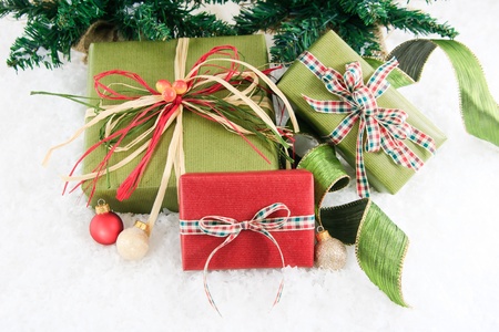 Festive red and green wrapped gifts are set in a snowy background with curly green ribbon and red, white and silver ornaments.の写真素材
