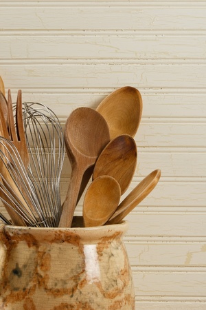 Wooden spoons and wire whisks in an old yellow and brown pot against a weathered wood background.の写真素材