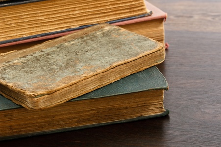 Heavily worn antique books piled on a wood tableの写真素材