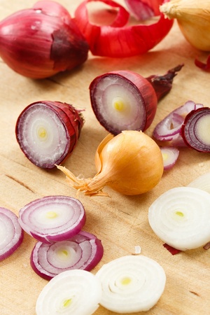 Sliced and whole red, yellow and white pearl onions scattered across a wood cutting board.の写真素材