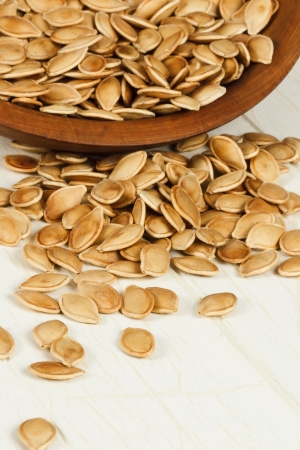 Healthy toasted pumpkin seeds spilling from a rustic wood bowl with focus on foreground seeds and copy space at bottomの写真素材