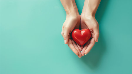 Hands holding a red heart against a pastel background, seen from above.の素材