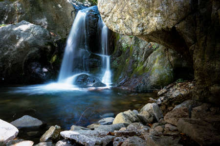Small mountain waterfall on the rocks covered with moss in the forestの写真素材