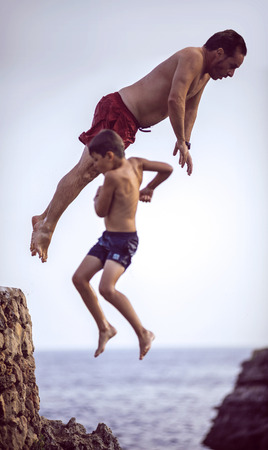 Menorca, Spain - September 8: Man and a kid jumping from cliff into the sea, on september 8, 2014, in Menorca, Balearic Islands, Spainのeditorial素材