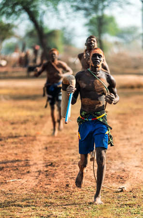 MUNDARI TRIBE, SOUTH SUDAN - MARCH 11, 2020: Young men with painted faces running together during training in savanna near Mundari Tribe village in South Sudan, Africaのeditorial素材