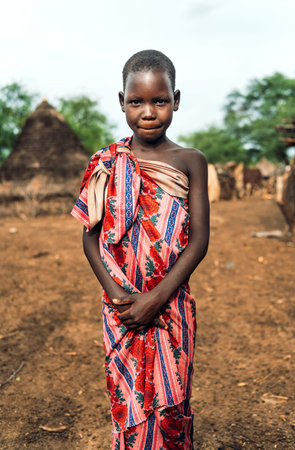 TOPOSA TRIBE, SOUTH SUDAN - MARCH 12, 2020: Girl wrapped in floral fabric looking and camera and...